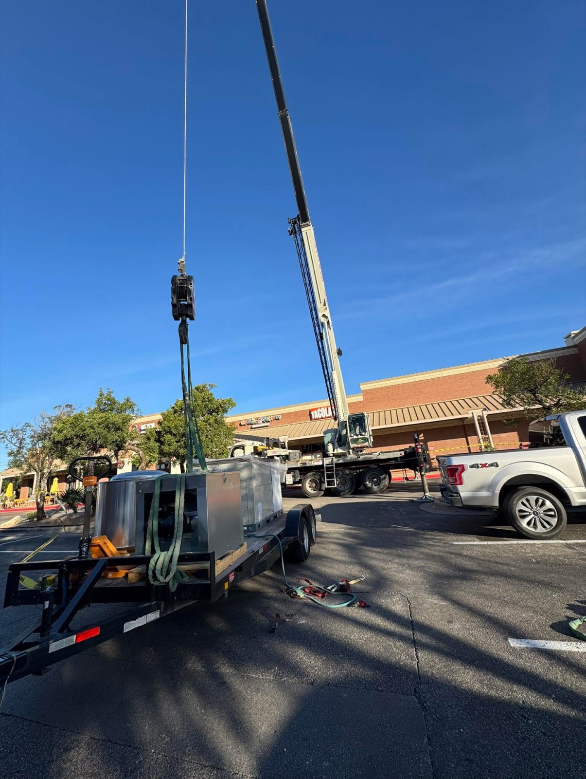Crane lifting a rooftop HVAC package unit into place at a commercial job site